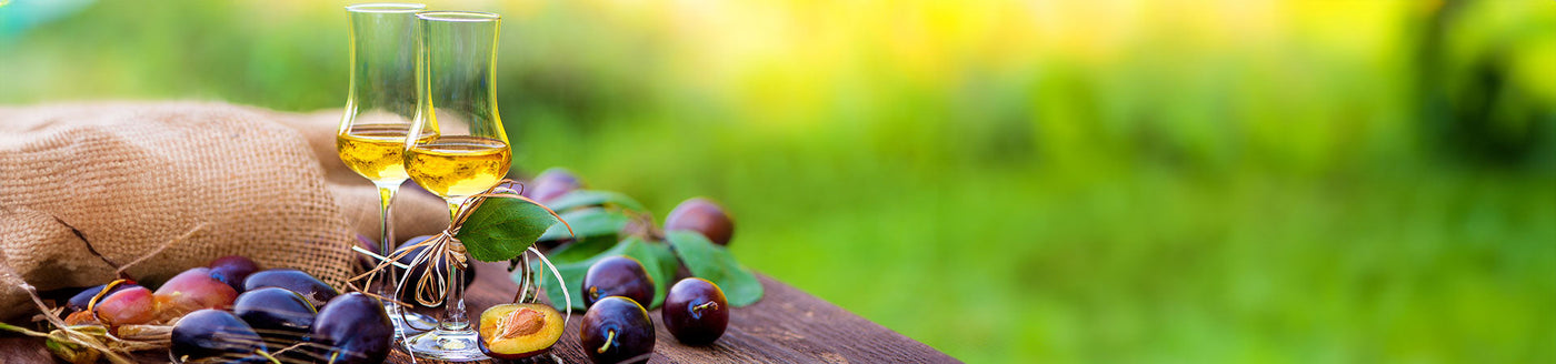 Verschiedene Obstbrände in Grappagläsern auf einem Holztisch neben Früchten