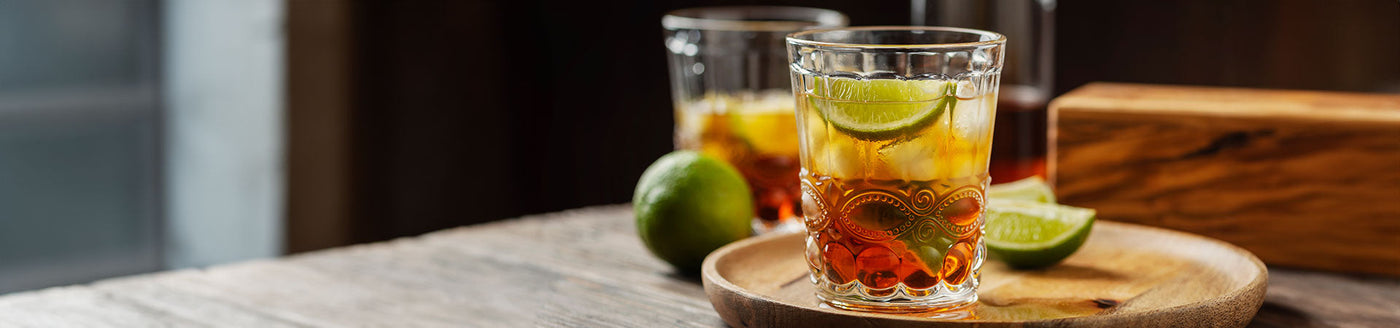 Cocktail-Gläser mit Spiced Rum, Cola und Limetten auf einem Holztisch