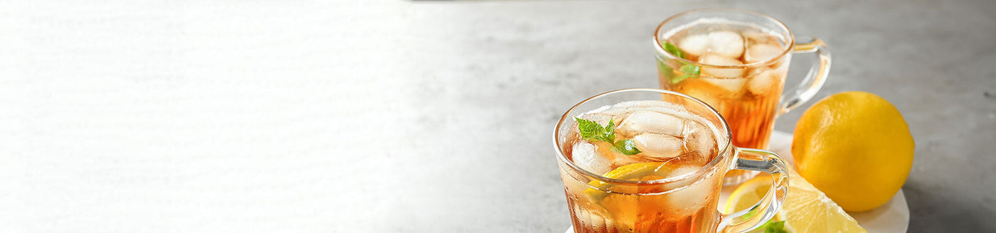 Mit Eistee und Eiswürfel gefüllte Gläser neben einer Zitrone