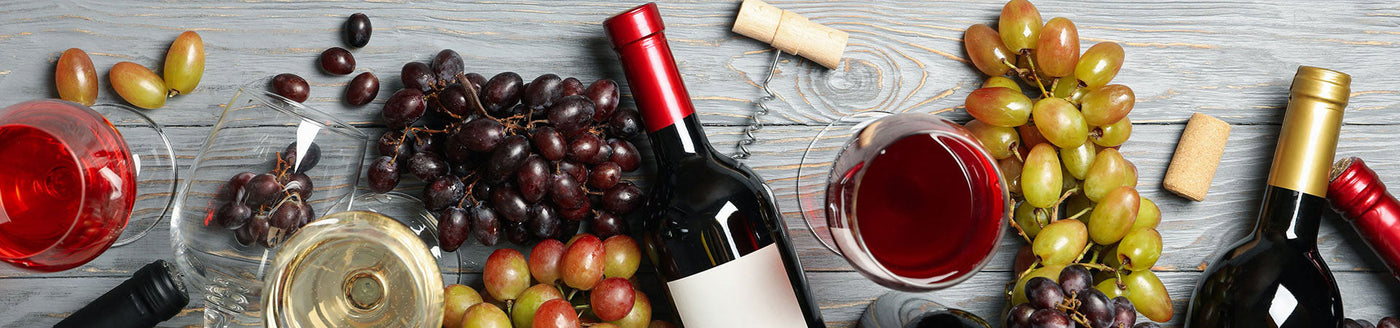 Liegende Weinflaschen mit Rotwein und Weißwein neben Weingläsern und Weintrauben