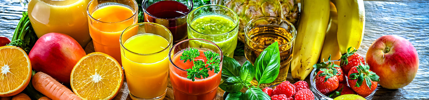 Saftgläser mit Johannisbeersaft und weiteren Säften neben einer Fruchtauswahl