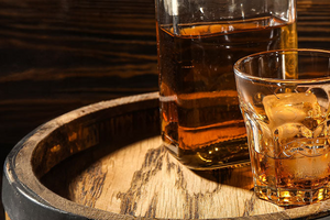 Whisky in einem Whiskyglas neben einer Whiskyflasche auf einem Holzfass