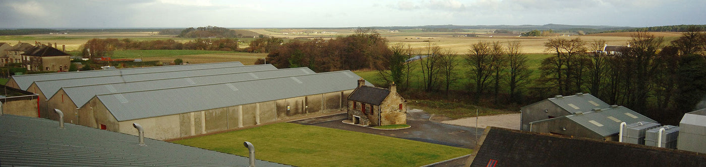 Blick auf die Ballantine’s Whisky Destillerie in Schottland, umgeben von Feldern und traditioneller Architektur