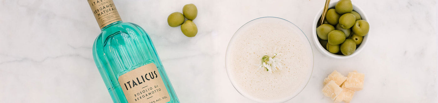 Italicus Aperitif mit Bergamotte, serviert mit Oliven, Käsewürfeln und cremigem Cocktail auf einer Marmorplatte