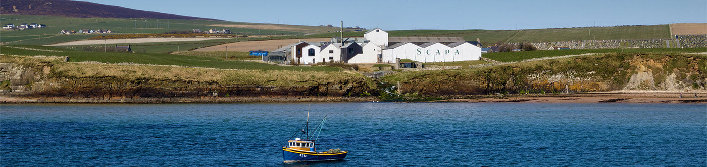 Scapa Single Malt Whisky Destillerie in Schottland mit Blick auf Meer und Fischerboot