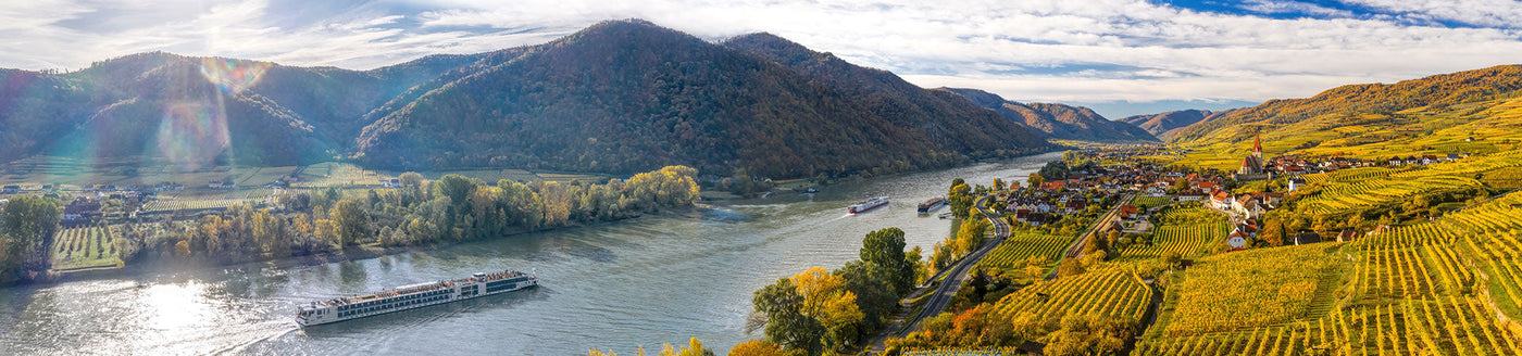 Panoramablick auf einen Fluss, der sich durch Hügel, Weinberge und ein kleines Dorf schlängelt, mit Booten auf dem Wasser.