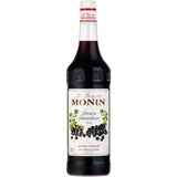 Eine 1-Liter-Flasche Monin Schwarze Johannisbeere Sirup mit weißem Etikett, verziert mit schwarzen Johannisbeeren und grünen Blättern - ideal, um Getränken wie Kir Royal eine fruchtige Note zu verleihen.